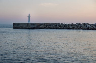 Deniz kenarındaki sete wavebreakers ile Seogwipo, Jeju Adası, Güney Kore şafak sırasında beyaz deniz feneri ile