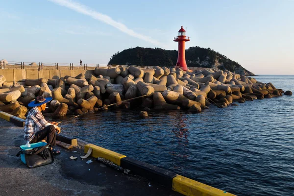 Pescador fumador al atardecer en el puerto con faro rojo en Seogwipo, isla de Jeju, Corea del Sur — Foto de Stock