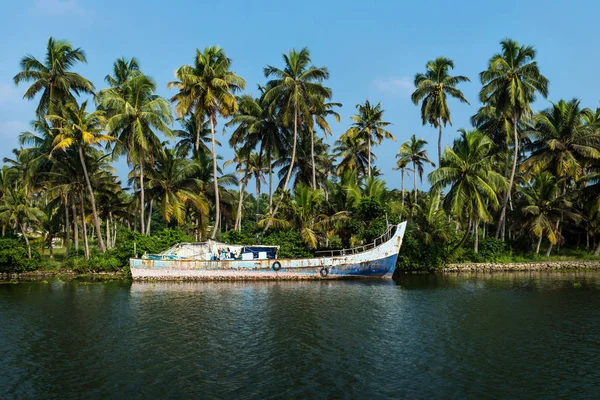 Abadoned ocean fishing boat along the canal Kerala backwaters shore with palm trees between Alappuzha and Kollam, India