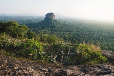 Lions Rock surrounded by forest and mountains in background during last sun in Sigiriya, Sri Lanka