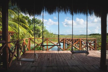Swings on pier along turquoise lagoon surrounded by tropical plants in Bacalar, Quintana Roo, Mexico