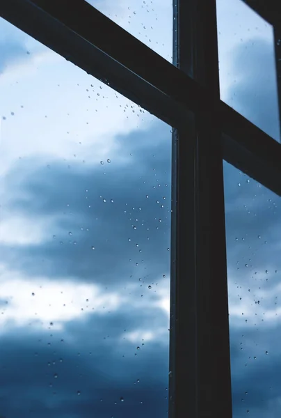 Window with rain droplets with view on dark blue cloudscape at home