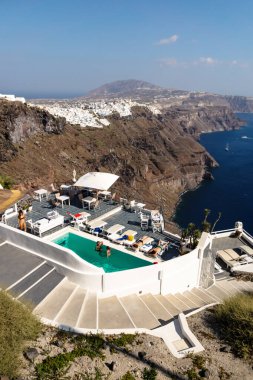 Imerovigli, Santorini, Yunanistan - 20 Temmuz 2014: Güneşli bir günde yüksek uçurumlara ve Fira köyüne bakan bir otel havuzunda konuklar