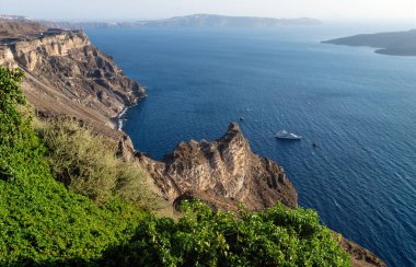 Son güneş, Santorini, Yunanistan 'da derin mavi okyanusa bakan yeşil çalıları olan kayalıklar