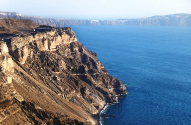 Günbatımında derin mavi okyanus boyunca uzanan volkanik kaya kayalıkları, Santorini, Yunanistan