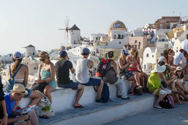 Oia, Santorini, Yunanistan - 22 Temmuz 2014: Arka planda yel değirmeni ve kubbeli kalede gün batımını bekleyen turist kalabalığı