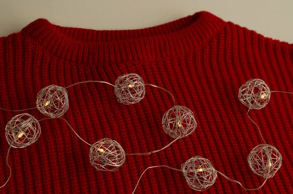 Beyaz yüzeyde kırmızı örülmüş bir kazak var. Spreciral formların ışıkları. Yeni yıl ve Noel konsepti. Moda rengi