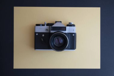 En üstten, koyu ve sarı arkaplandaki klasik fotoğraf makinesinin görüntüsünü al. Mercekli metal gümüş ve plastik siyah çerçeve.