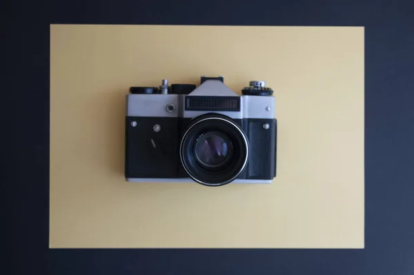 En üstten, koyu ve sarı arkaplandaki klasik fotoğraf makinesinin görüntüsünü al. Mercekli metal gümüş ve plastik siyah çerçeve.