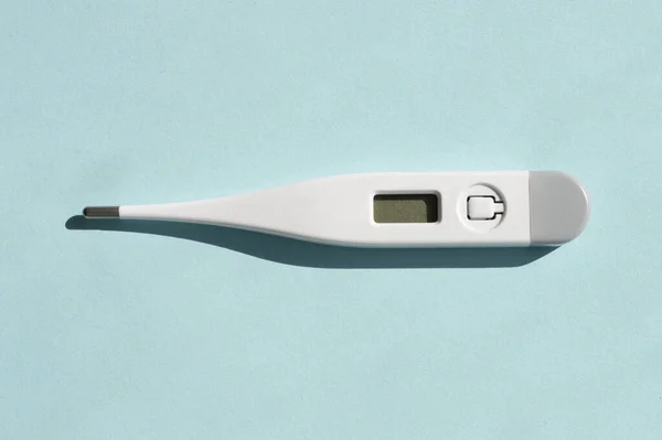 Güneşli açık mavi arka planda gölgeli bir plastik beyaz elektronik termometre. Sağlık tedavisi kavramı.