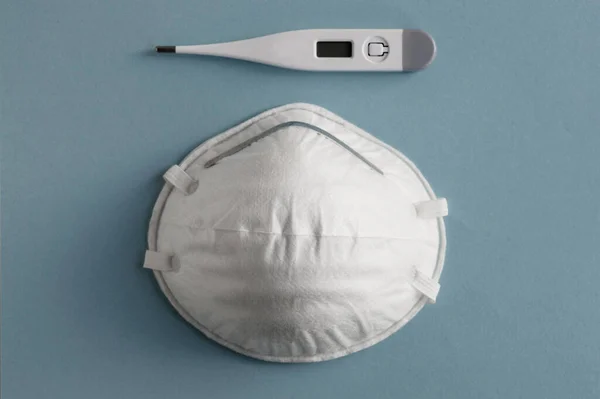 Açık mavi arka planda beyaz termometre ve tıbbi maske. Kirliliğe, virüse ve koronavirüse karşı koruma. Sağlık hizmeti kavramı.