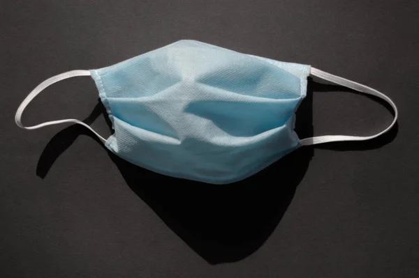 Koyu siyah arka planda açık mavi tek kullanımlık yüz maskesi virüse karşı covid-2019. Minimalist sağlık konsepti, karantina, koronavirüsü durdurun..