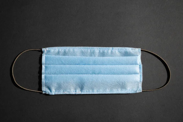 Açık mavi tıbbi tek kullanımlık yüz maskesi ve siyah şeritli siyah arka plan, 2019 virüsüne karşı. Minimalist sağlık konsepti, karantina, koronavirüsü durdurun..