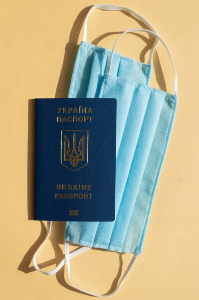 Açık sarı arka planda iki açık mavi tıbbi maske üzerinde Ukrayna 'nın yabancı pasaportunun dikey fotoğrafı virüse karşı covid-2019. Heath care konsepti, koronavirüsü durdurun..