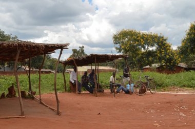 LILONGWE, MALAWI, AFRICA - 1 Nisan 2018: Parlak yol sahnesi, altı Afrikalı adam dünyanın en yoksul ülkelerinden birinde yol boyunca ahşap inşaat altında oturuyor.
