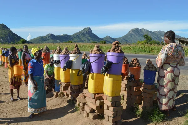 LILONGWE, MALAWI, AFRICA - 25 Mart 2018: Dört Afrikalı kadın Dedza yolu boyunca gülümsüyor ve patates satıyor. Mutlu atmosfer, parlak mor, kırmızı, turuncu ve sarı renkler.