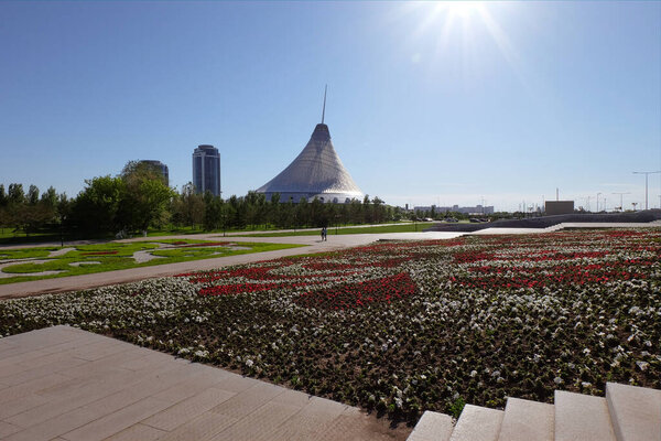 NUR-SULTAN, ASTANA, KAZAKHSTAN - JUNE 3, 2015: City view with Khan Shatyr Entertainment Center on the background. Empty city view with white and red flowers on the flowerbed
