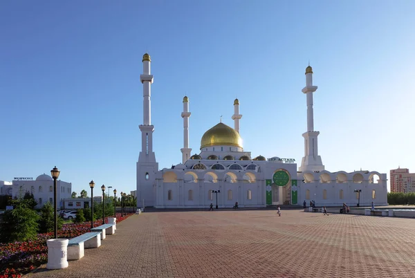 NUR-SULTAN, ASTANA, KAZAKHSTAN - 3 Haziran 2015: Altın kubbeli Beyaz Nur Astana Camii. Güneşli bir günde kırmızı ve mor petunya çiçekli boş bir meydan.
