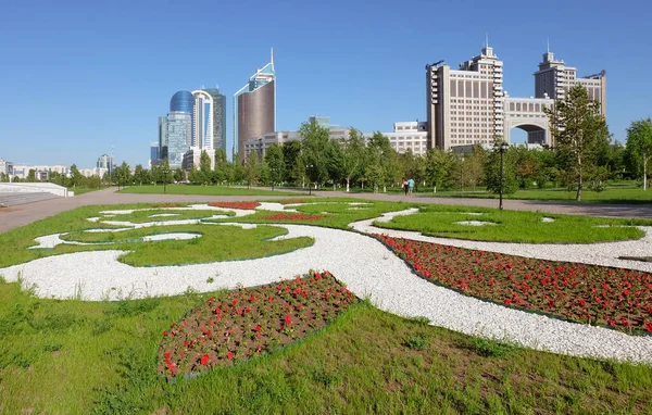 NUR-SULTAN, ASTANA, KAZAKHSTAN - JUNE 3, 2015: City view to the flowerbed with ornament of petunia flowers with skyscapper buildings and KazMunayGas on the background at day time — Stock Photo, Image