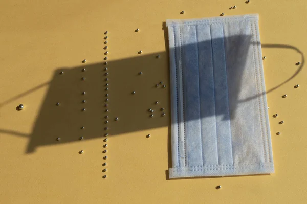 Mavi yüzlü tıbbi maske ve sarı arka planda küçük gümüş boncuklar. Koronavirüsün yayılması ve durdurulması hakkında. Sanat kavramsal fikri.