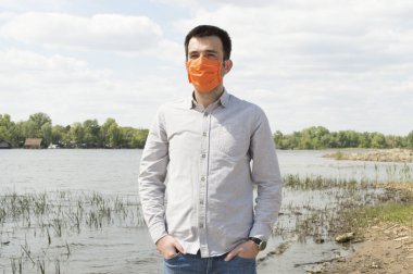 Açık gri gömlekli ve parlak turuncu yüzlü Türk adam Ukrayna 'nın Kyiv kentindeki Dinyeper nehrinin kıyısında. Karantina süresince sağlık koruma kavramları. Virüsü durdur, koronavirüsü