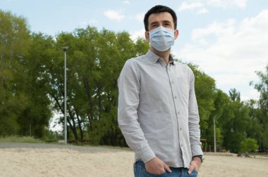 Ukrayna 'nın başkenti Kyiv yakınlarındaki Dinyeper nehrinin sahilinde karantina zamanında açık gri gömlekli ve koronavirüse karşı koruyucu mavi maskeli bir Türk. Sağlık hizmeti kavramı
