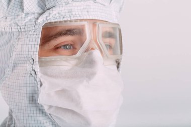 Tıbbi maske, koruyucu gözlük ve kimyasal elbise takmış Avrupalı bir erkek doktorun portresi.
