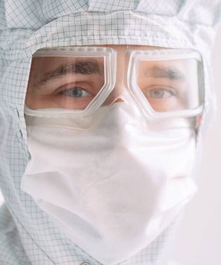 Tıbbi maske, koruyucu gözlük ve kimyasal elbise takmış Avrupalı bir erkek doktorun portresi.