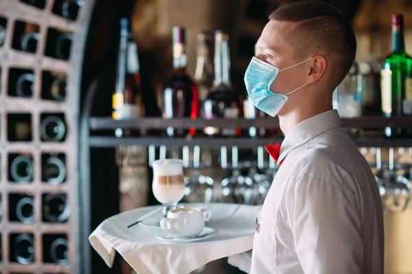 一个戴着医疗面罩 长相像欧洲人的侍者端着拿铁咖啡 — 图库照片