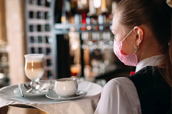 一位戴着医疗面罩的欧洲女服务员端着拿铁咖啡 — 图库照片