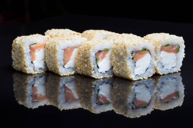Sushi dürümleri siyah arkaplanda susamlı Chizu sallar.