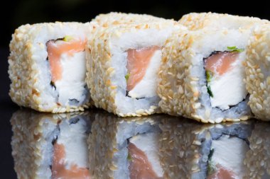 Sushi dürümleri siyah arkaplanda susamlı Chizu sallar.