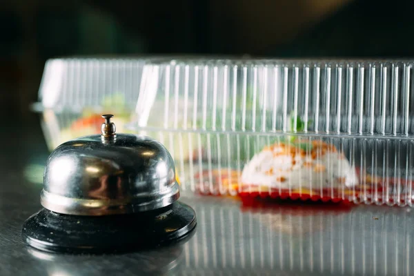 food delivery. distribution table in a restaurant with a metal bell. food in plastic containers. Panna cotta and vegetable salad in a plastic disposable containers