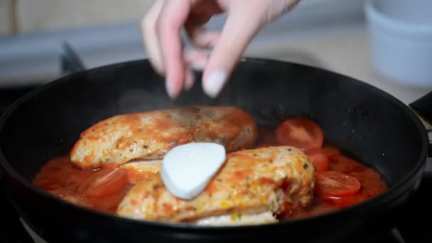 Uma mulher cozinha frango em molho de tomate. Coloque pedaços de mussarela no frango. — Vídeo de Stock