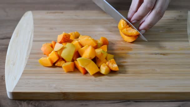 Vrouwelijke handen snijden abrikoos op houten bord — Stockvideo