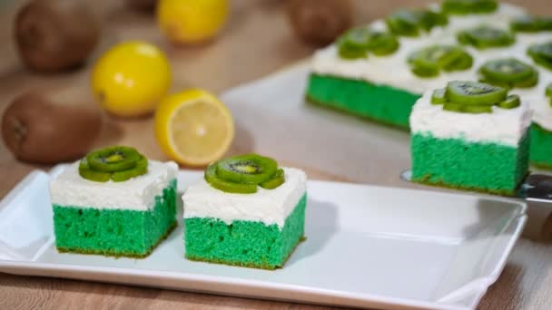 Выложить в белую тарелку зеленый мягкий торт с взбитыми сливками и посыпать киви — стоковое видео