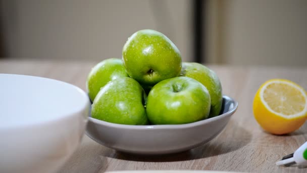 Жінка бере свіже зелене яблуко з фруктової миски на кухні — стокове відео