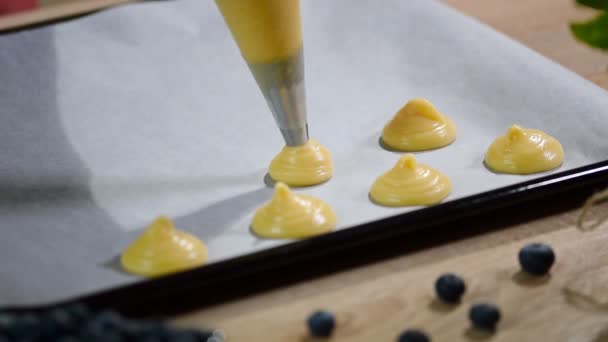 Masa choux de tubería para profiteroles sobre papel de hornear — Vídeos de Stock