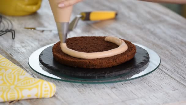 Confectioner Girl Aplicar crema de chocolate a través de una bolsa de pastelería en un pastel de esponja de chocolate . — Vídeos de Stock