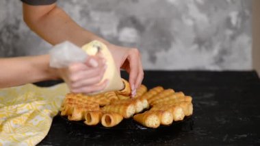 Kadın, kremayı boynuz rulosunun iki ucuna da borular. Kremalı börek yapan bir kadın..