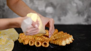Kadın, kremayı boynuz rulosunun iki ucuna da borular. Kremalı börek yapan bir kadın..