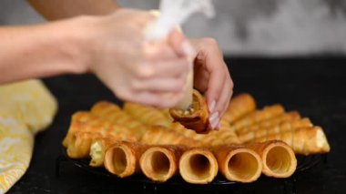 Kadın, kremayı boynuz rulosunun iki ucuna da borular. Kremalı börek yapan bir kadın..