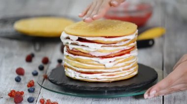 Sünger tabakaları lezzetli kek yapma kadın pasta şef eller, dönen kek standı kullanarak krem şanti ve berry reçel.