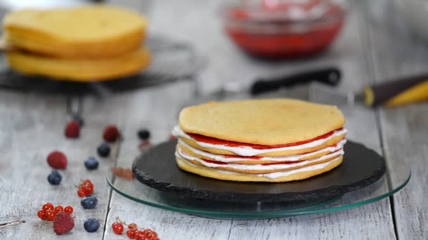 Handen van vrouwelijke banketbakker het maken van heerlijke taart van spons lagen, slagroom en Berry jam met behulp van roterende cake stand. — Stockvideo
