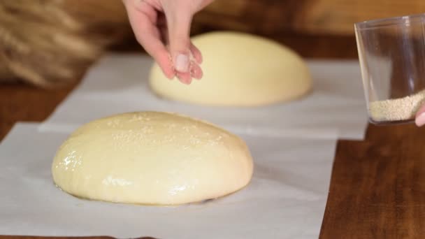 Hand sprider sesamfrön på degen. Bakning av traditionellt hembakat bröd. — Stockvideo