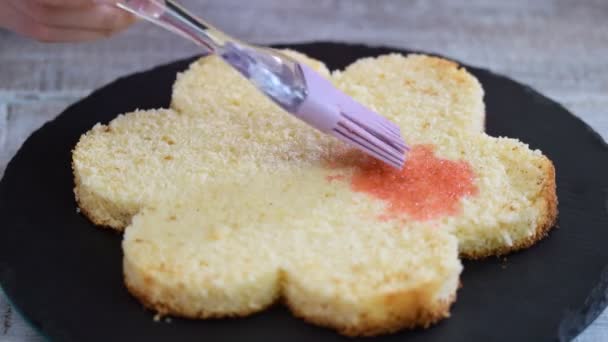 Namoczenie warstwy tortu gąbczastego syropem. Cukiernik robi różowe ciasto w kształcie kwiatu. — Wideo stockowe
