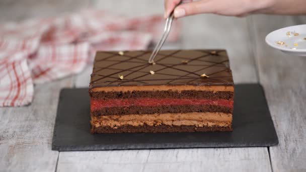 Gros plan sur les mains d'un chef pâtissier décore gâteau au chocolat avec feuille d'or . — Video