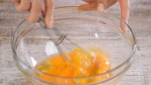 Beating eggs with whisk in glass bowl, on a table. Close-up. — Stock Video