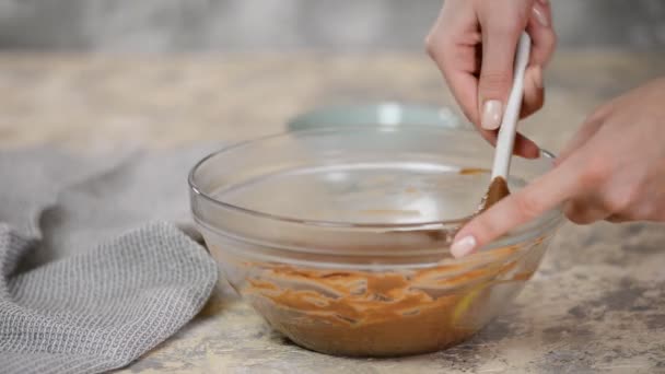 Mujer revolviendo deliciosa crema de chocolate en un tazón con batidor en la mesa . — Vídeos de Stock