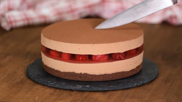 Vrouwen handen snijden de heerlijke chocolade mousse cake met frambozen gelei. — Stockvideo